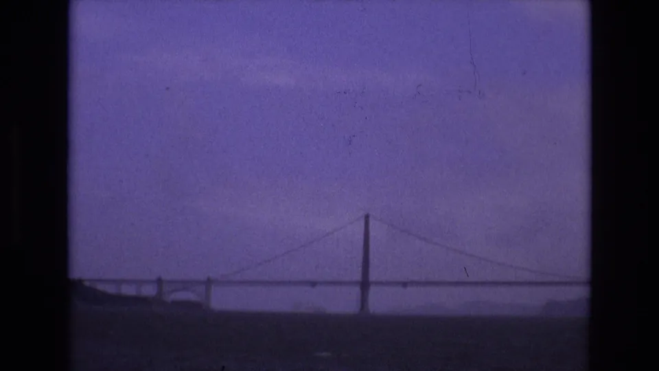 A distant suspension bridge spans the water in this purple-tinted 1973 San Francisco home-movie frame.