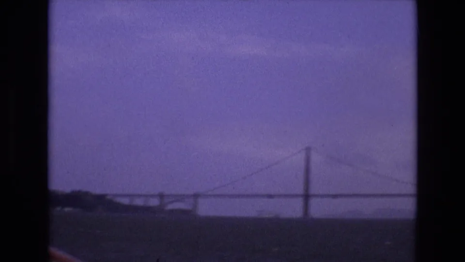 Soft-focus 8mm frame showing the distant bridge, water, and low shoreline in the supplied 1973 San Francisco Bay context.