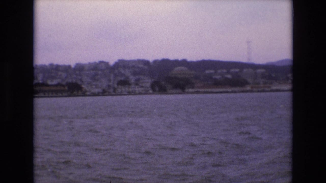 Rippling water with a distant urban hillside and waterfront structures.