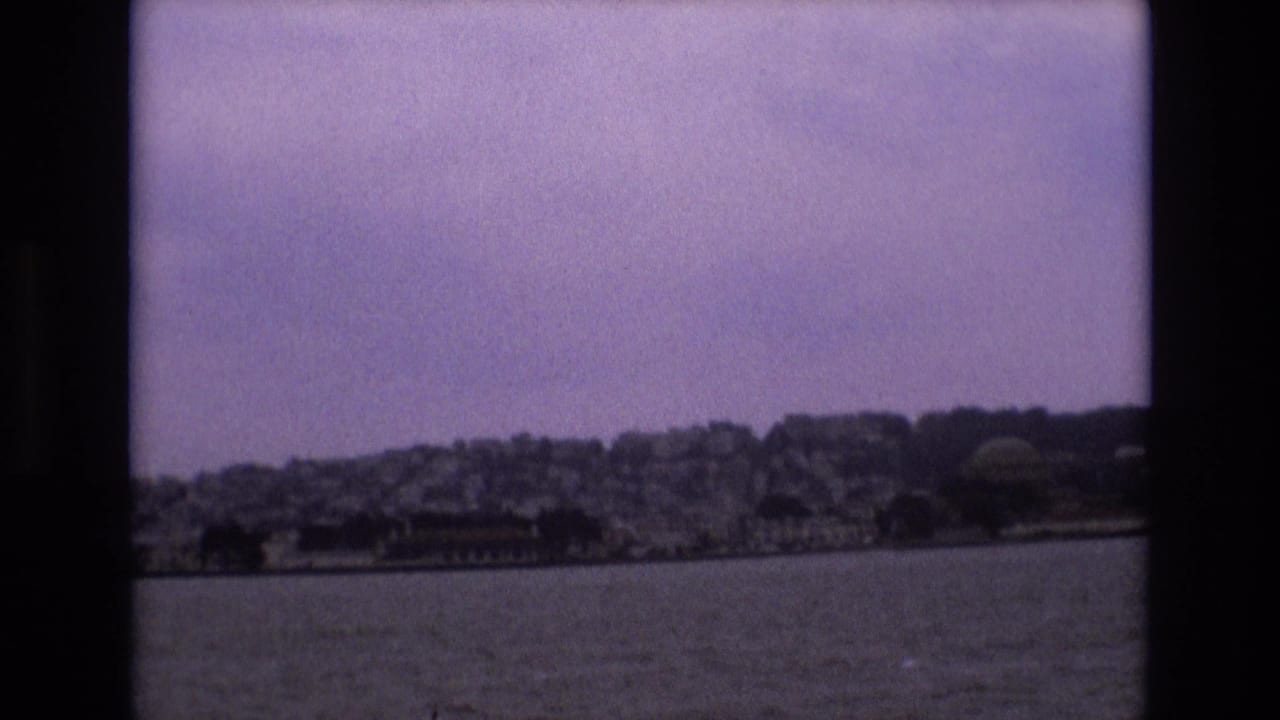 1973 8mm view from a boat looking across bay water toward San Francisco hillside buildings under a hazy purple-tinted sky.