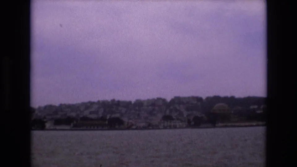 Boat-level 8mm view of San Francisco’s waterfront and hillside buildings, with rippled water in the foreground and faded color in the sky.