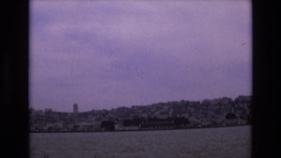 Final 1973 frame looking from the bay toward San Francisco’s distant hillside cityscape, with soft focus, grain, and purple color fading.
