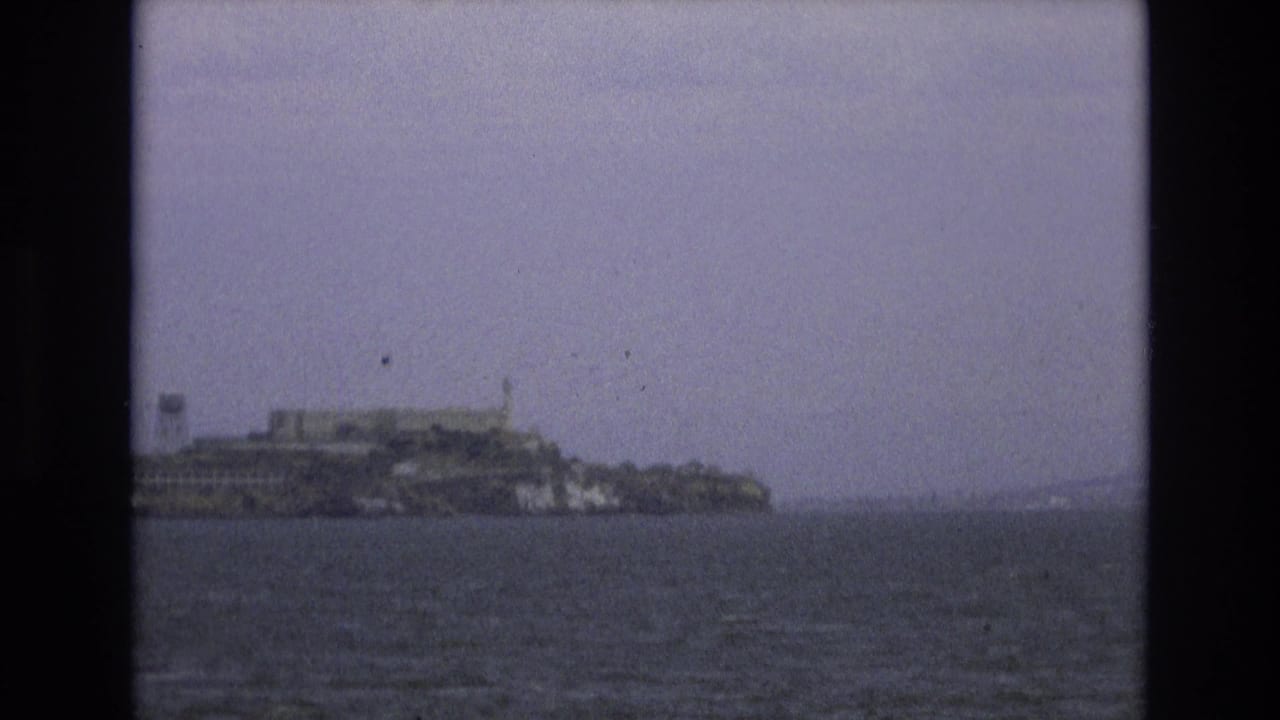Alcatraz Island seen across San Francisco Bay water under an overcast sky.