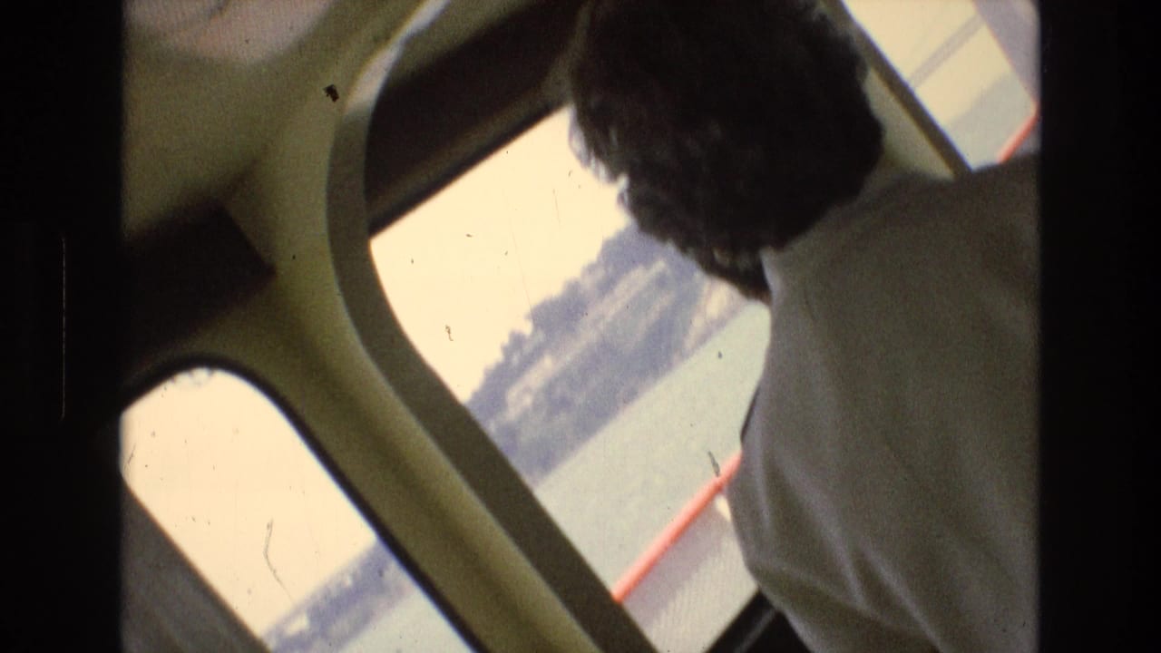 1973 San Francisco Bay home-movie frame from inside a boat cabin, with a passenger looking out toward the water and shoreline.