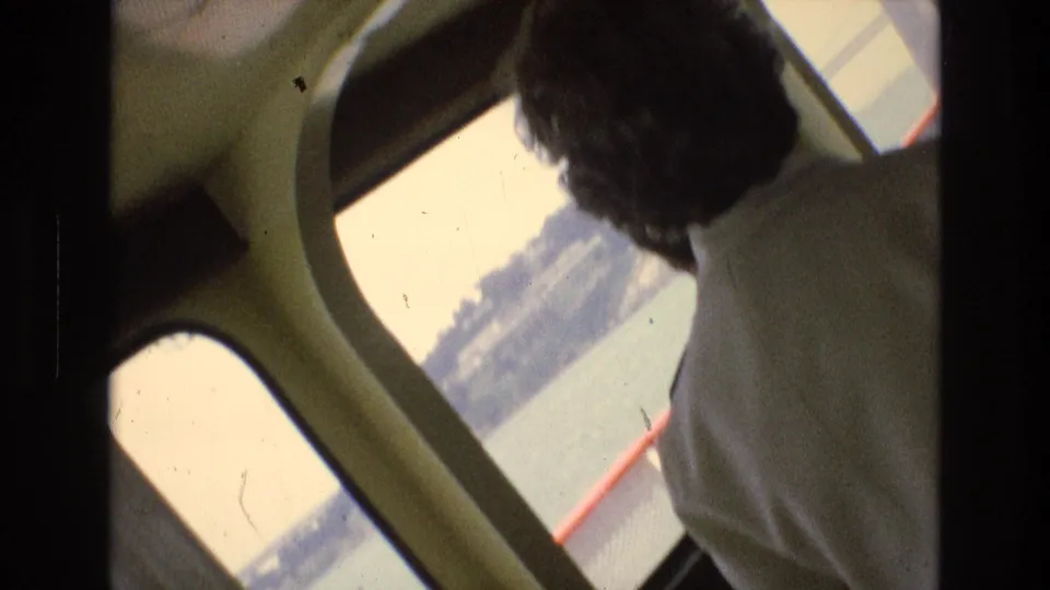 1973 San Francisco Bay home-movie frame from inside a boat cabin, with a passenger looking out toward the water and shoreline.