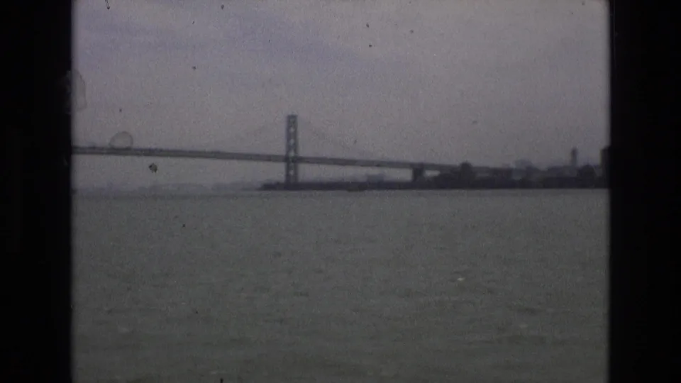 1973 8mm home-movie frame showing the Golden Gate Bridge across San Francisco Bay beneath a cloudy sky.