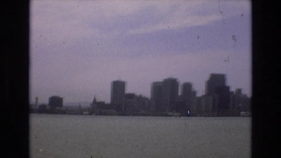 1973 8mm frame of San Francisco high-rises and shoreline buildings viewed from across bay water, with a soft, faded home-movie look.