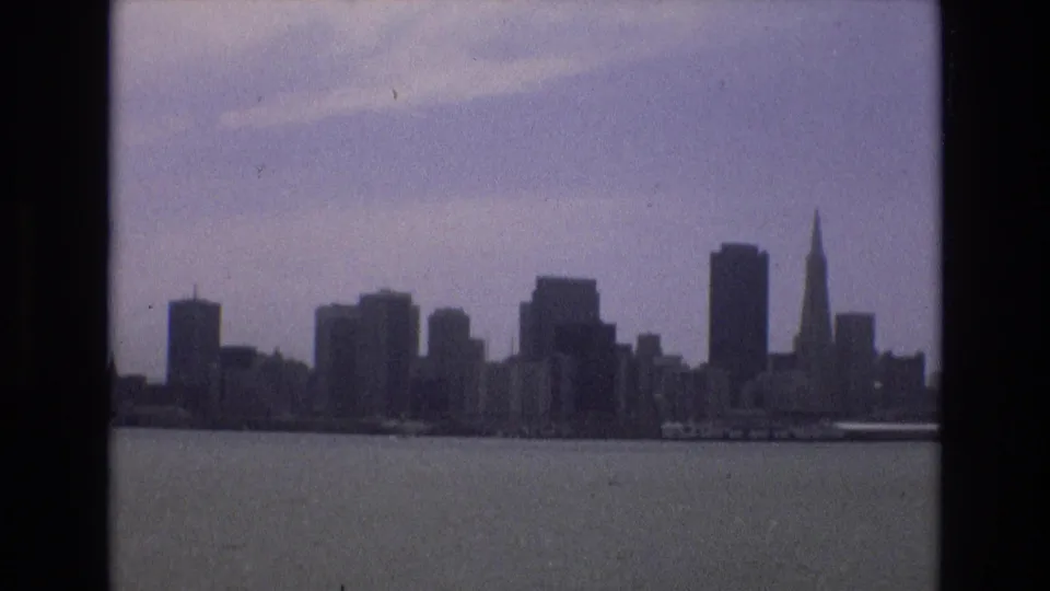 1973 San Francisco skyline across the bay, with the Transamerica Pyramid and surrounding downtown towers silhouetted against a hazy sky.