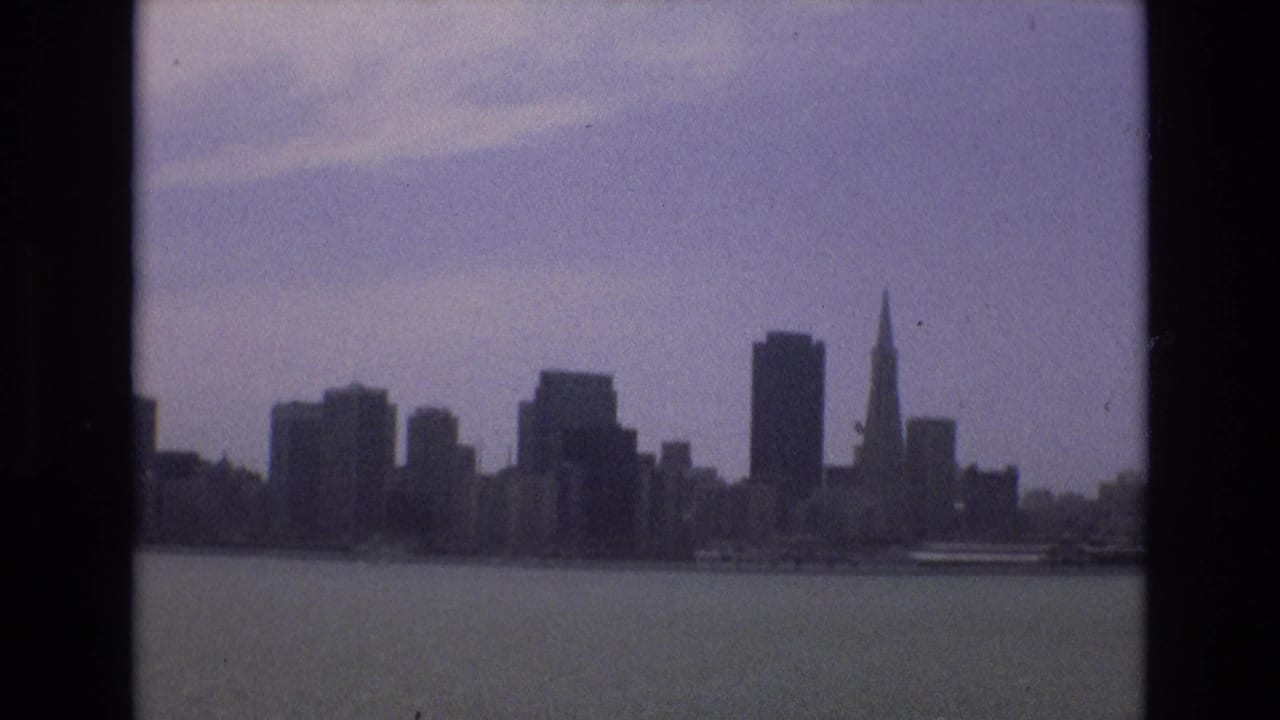 Distant San Francisco skyline across calm bay water under a hazy sky.