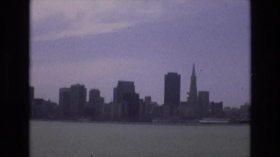 A 1973 8mm home-movie view of the San Francisco skyline across bay water, with high-rises and the Transamerica Pyramid visible in soft focus.