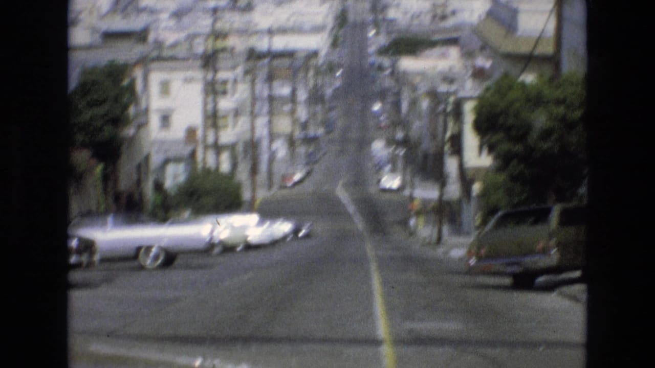 1973 San Francisco street view looking uphill past parked classic cars, apartment buildings, trees, and overhead utility wires.