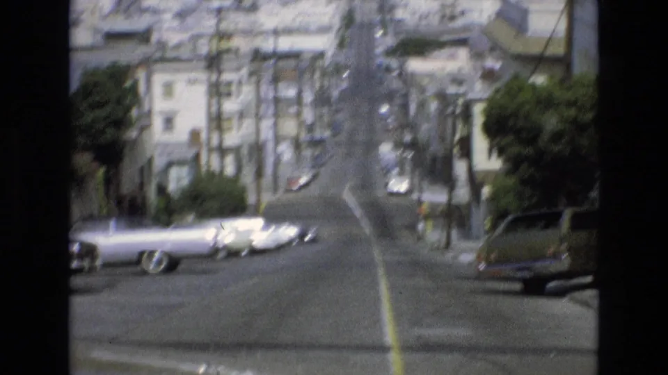 1973 San Francisco street view looking uphill past parked classic cars, apartment buildings, trees, and overhead utility wires.