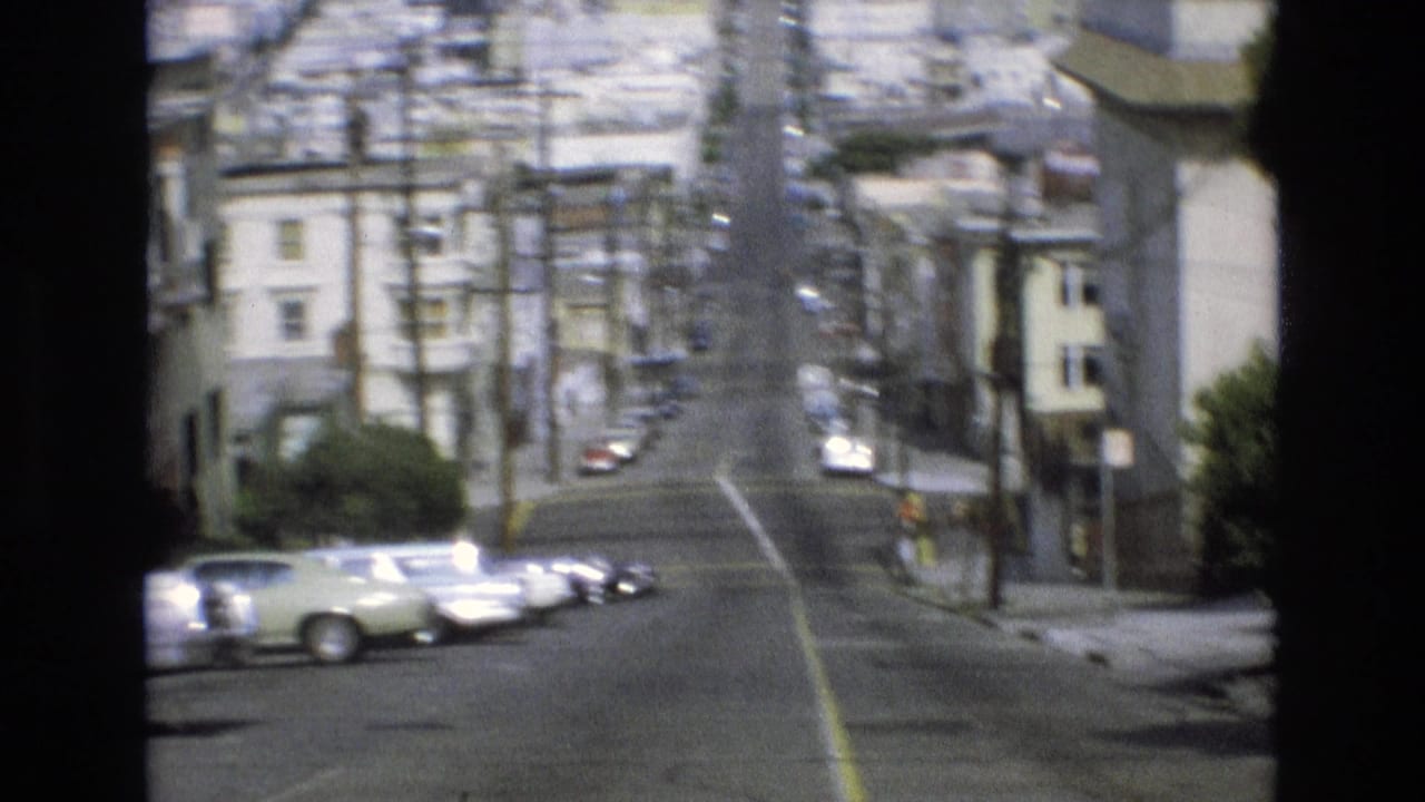 Steep San Francisco street with parked cars, utility poles, and residential buildings.