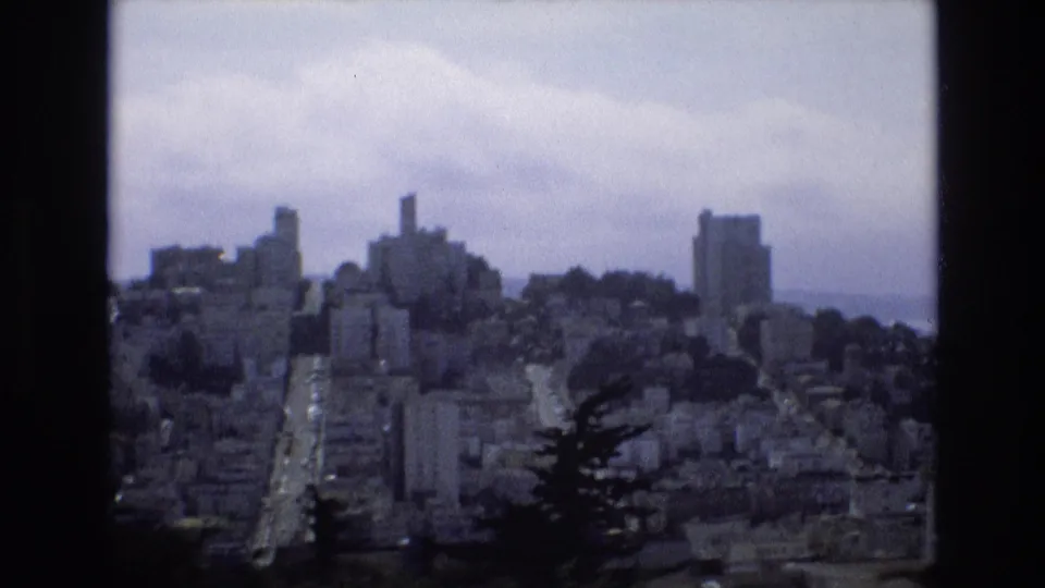 Wide 1973 San Francisco home-movie view of dense hillside architecture and a distant city skyline under a gray, overcast sky.
