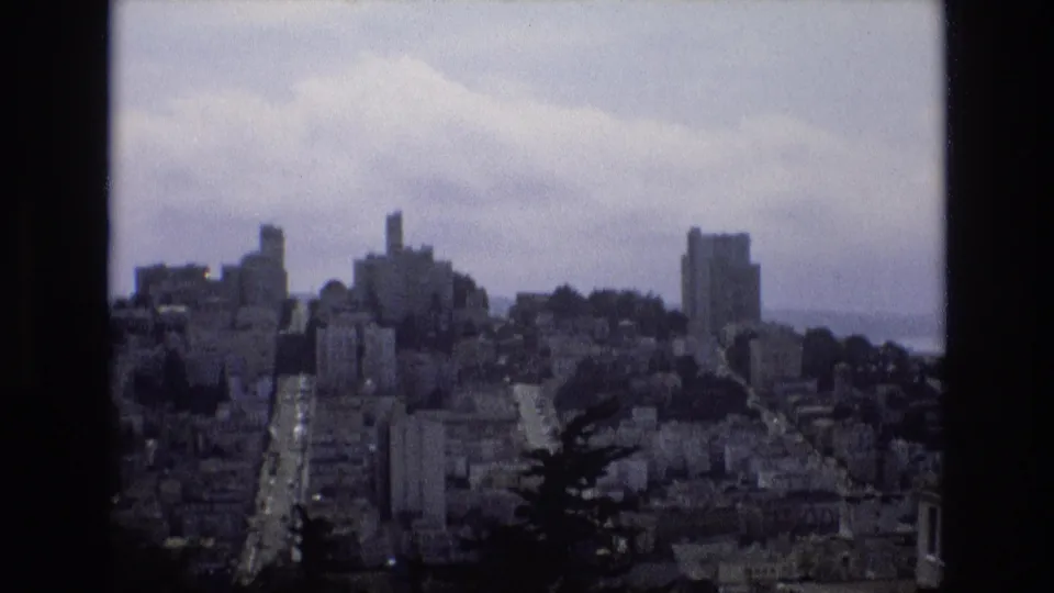The San Francisco city view remains framed by dark film edges, with clustered hillside buildings, a prominent street, and a muted cloudy sky above.