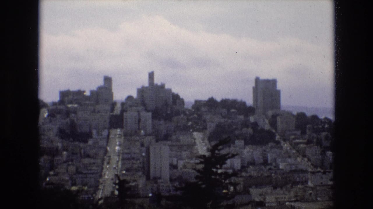 Elevated city view with hillside buildings and roads under a hazy sky.