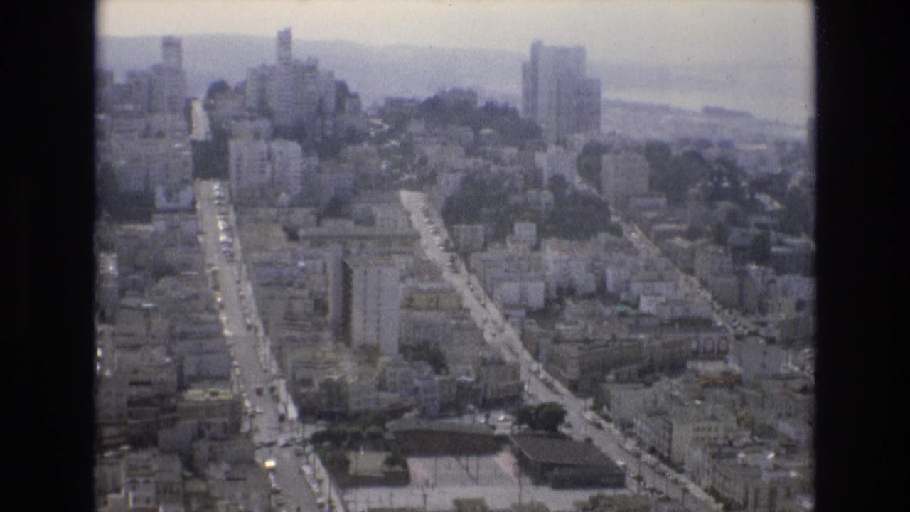 Aerial city view with long streets, towers, and water beyond.