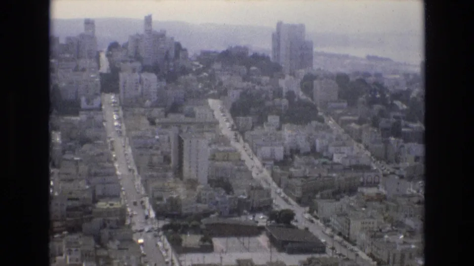 1973 San Francisco aerial view showing long corridors of street traffic, compact urban blocks, high-rise buildings, and hazy water beyond the city.