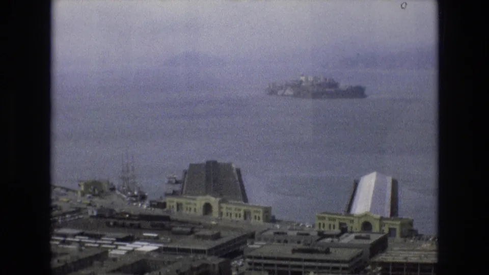 1973 8mm home-movie frame looking across San Francisco Bay from the Embarcadero area toward distant Alcatraz under a hazy sky.