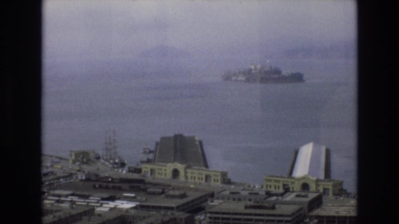 A hazy 1973 San Francisco waterfront view shows Alcatraz across the bay, with pier structures and ferry terminal architecture in the foreground.