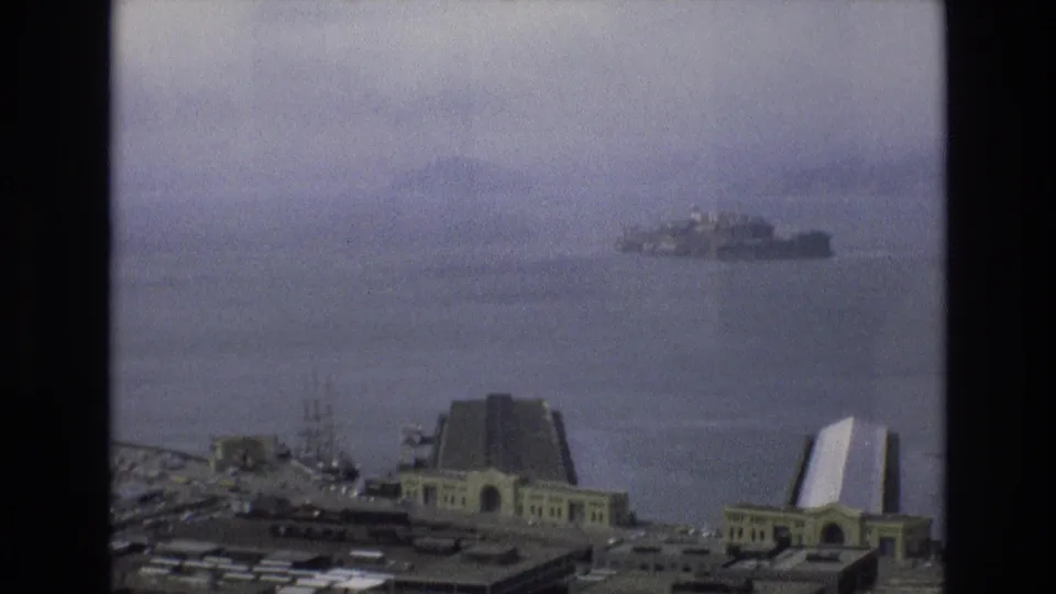 1973 San Francisco bayfront view from an elevated position, with shoreline buildings in the foreground and Alcatraz Island visible in the distance.
