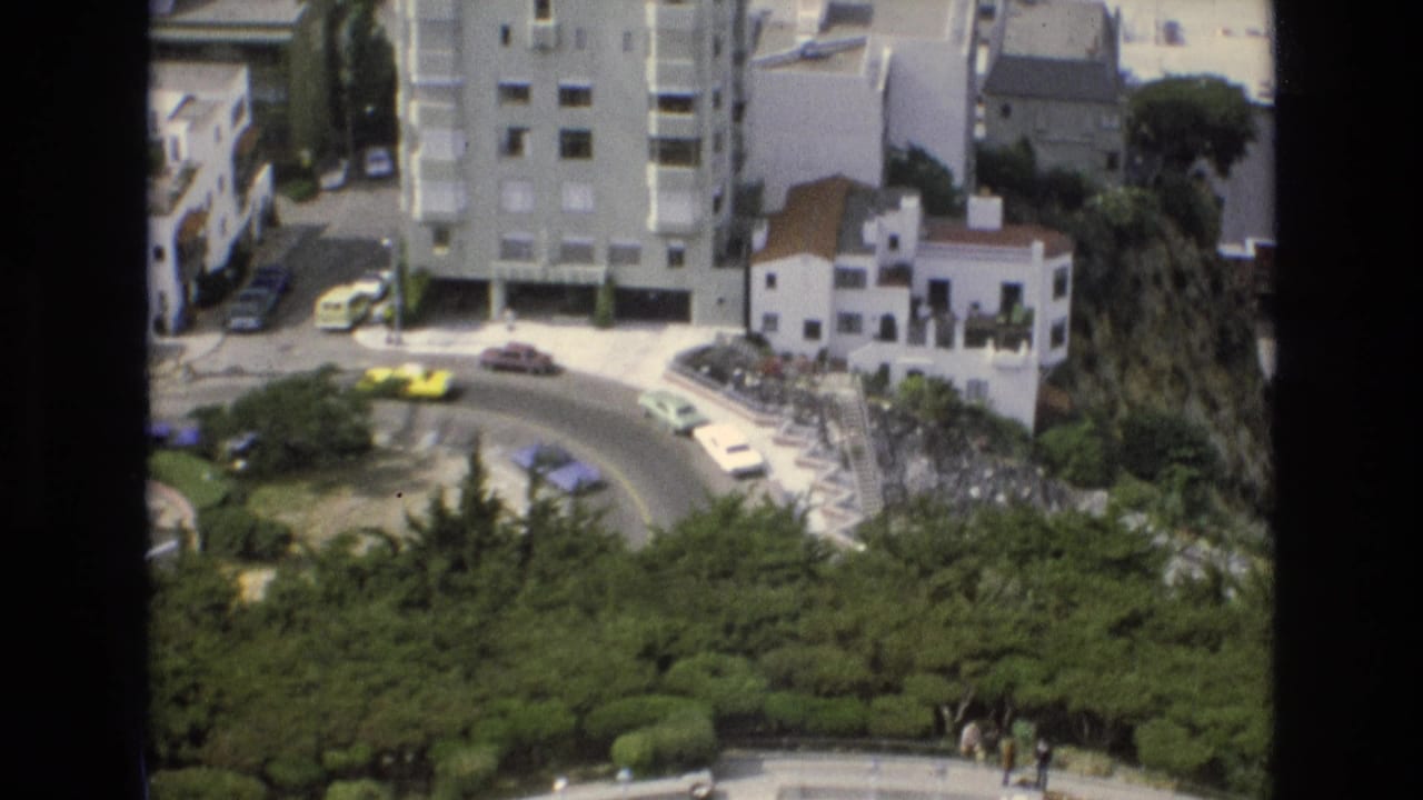 Elevated view of a curved city street with cars, buildings, and greenery.