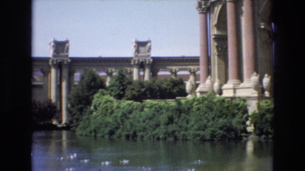1973 8mm view of San Francisco's Palace of Fine Arts colonnade across a lagoon with ducks and dense greenery in the foreground.