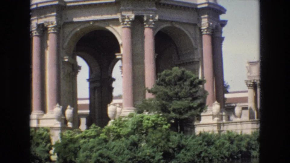 Final 1973 8mm frame on the Palace of Fine Arts rotunda in San Francisco, showing column details, archways, thick greenery, and a small tree near the lagoon.