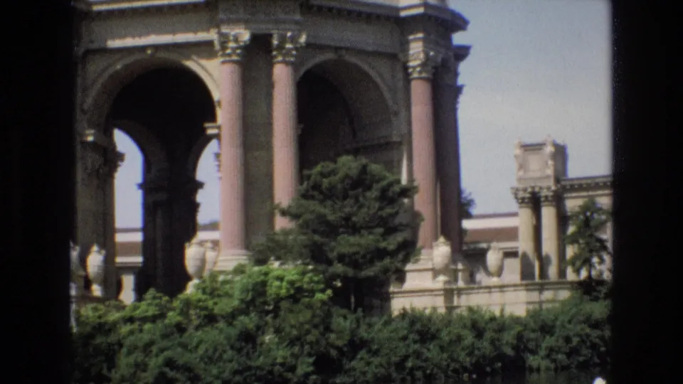 1973 8mm San Francisco footage shows the Palace of Fine Arts rotunda with tall columns, archways, shrubs, and the reflecting pool in the foreground.