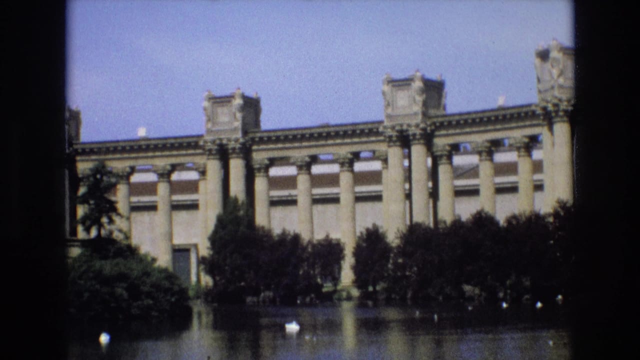 1973 San Francisco home-movie frame showing a large columned stone structure across calm water, partly screened by dark foliage and film-frame edges.