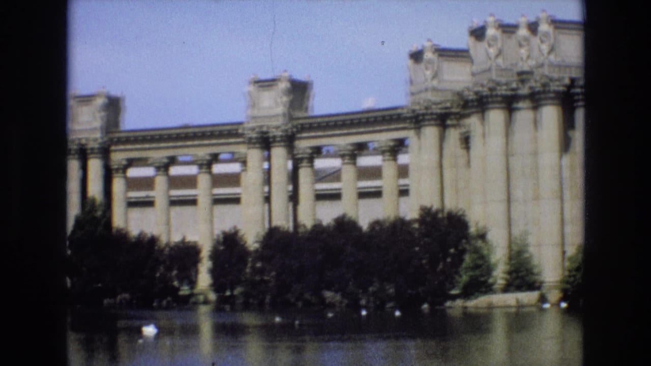 Long neoclassical facade with columns, trees, and water in front.