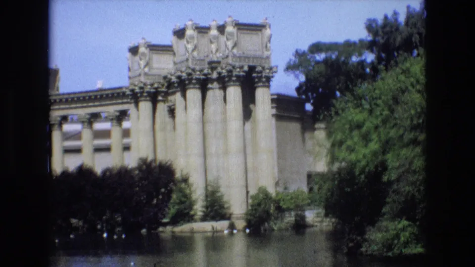 1973 San Francisco 8mm frame showing a columned classical-style structure at the edge of a lake, partly obscured by trees and dark contact-sheet borders.
