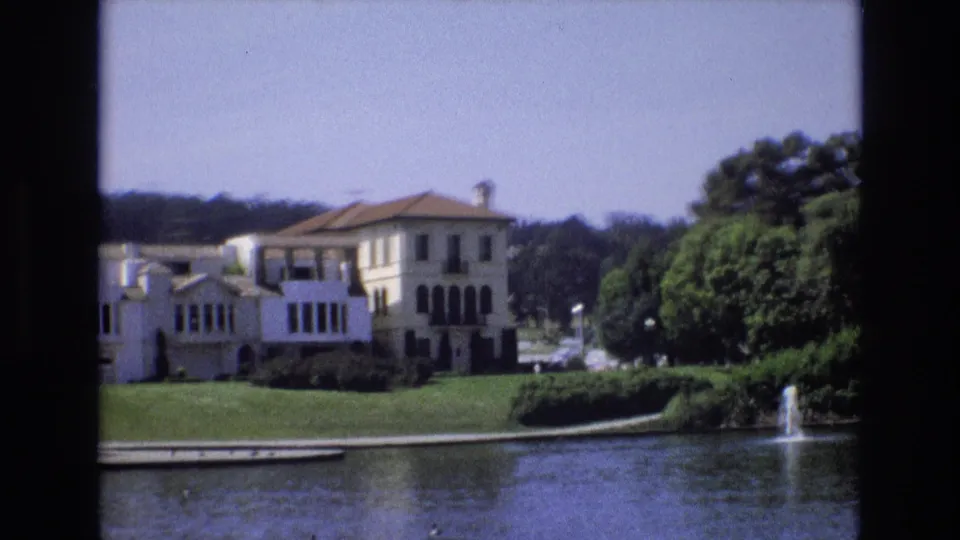 1973 San Francisco 8mm frame showing the mansion across the water, with broad lawn, shrubs, trees, and a small fountain visible to the right.