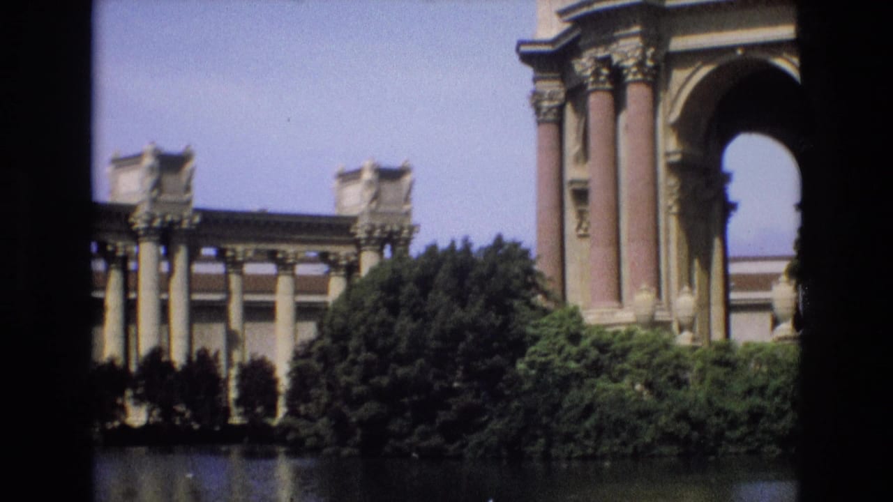 1973 8mm view of the Palace of Fine Arts in San Francisco, with columns, an arch, trees, shrubs, and water framed by dark film borders.