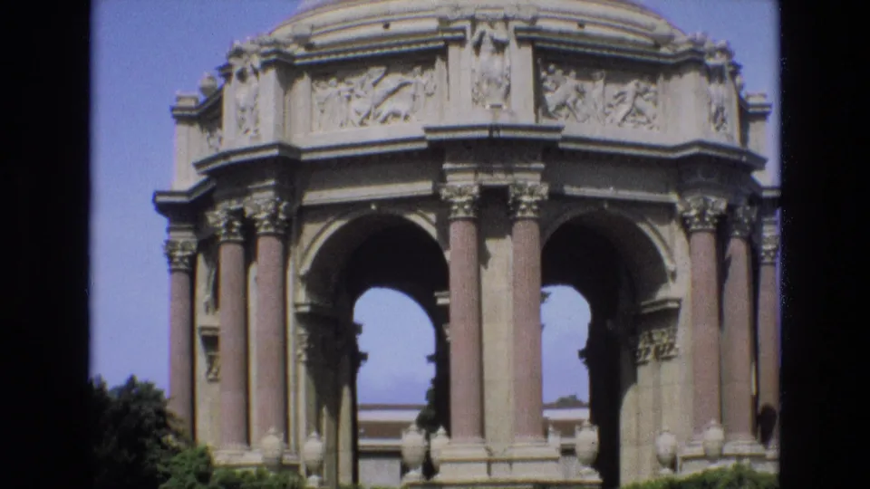 1973 8mm view of the Palace of Fine Arts in San Francisco, centered on the ornate rotunda, Corinthian-style columns, arched openings, frieze details, and surrounding bushes.