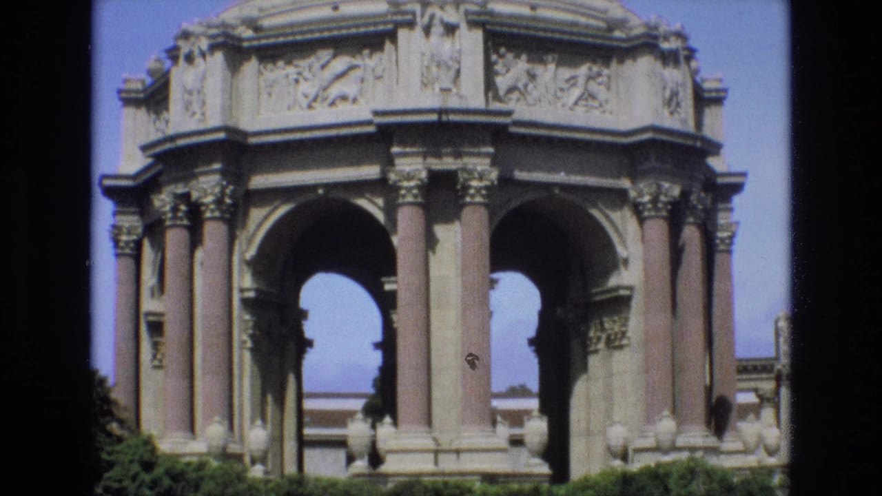 1973 San Francisco home-movie frame showing the Palace of Fine Arts rotunda, arched openings, columns, foreground shrubs, and dark film borders.