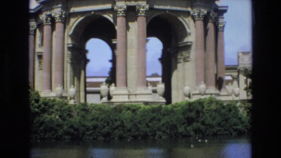 1973 San Francisco home-movie frame showing a closer cropped view of the Palace of Fine Arts arches, columns, foreground hedge, and lagoon surface.