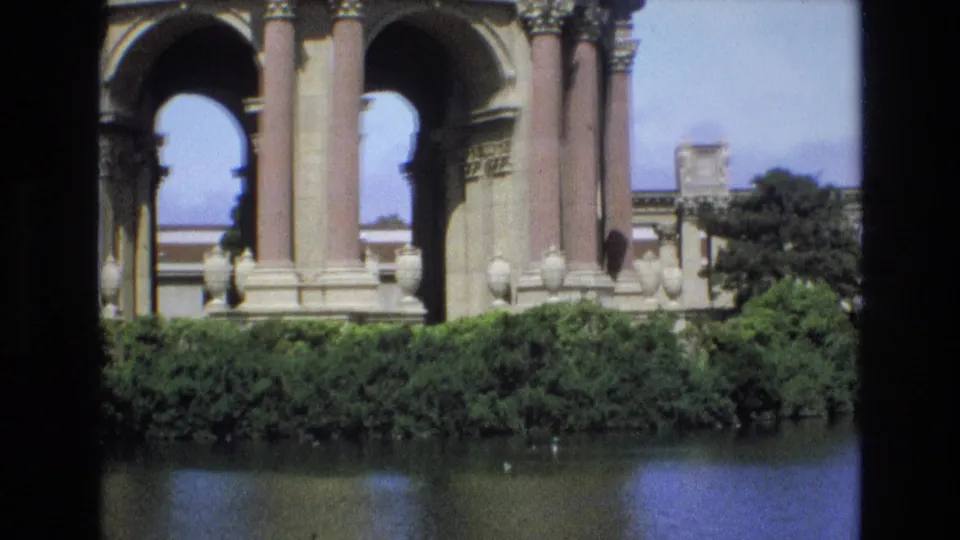 1973 San Francisco frame showing the Palace of Fine Arts colonnade and arches, clipped greenery, lagoon reflections, and the edge of adjacent structures.