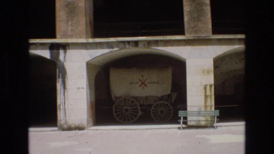 1973 San Francisco 8mm frame showing a covered wagon with a red cross-like marking parked under a concrete archway, with a bench and barrel nearby.