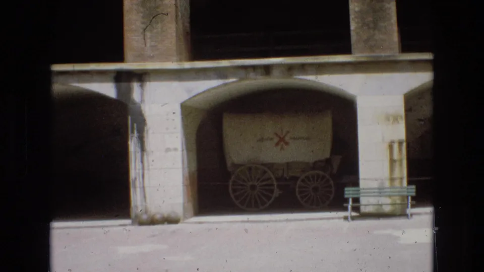 1973 San Francisco 8mm frame with a covered wagon under a concrete bay, a red cross-like symbol on the wagon cover, and a bench at the right edge.
