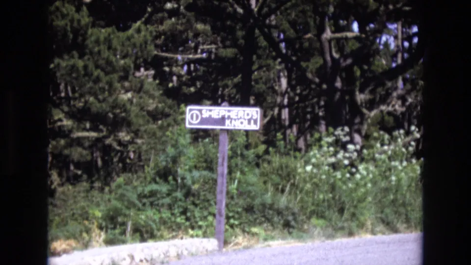Final 1973 San Francisco-area frame holding on the Shepherd's Knoll roadside sign, with shrubs and tall trees filling the background.