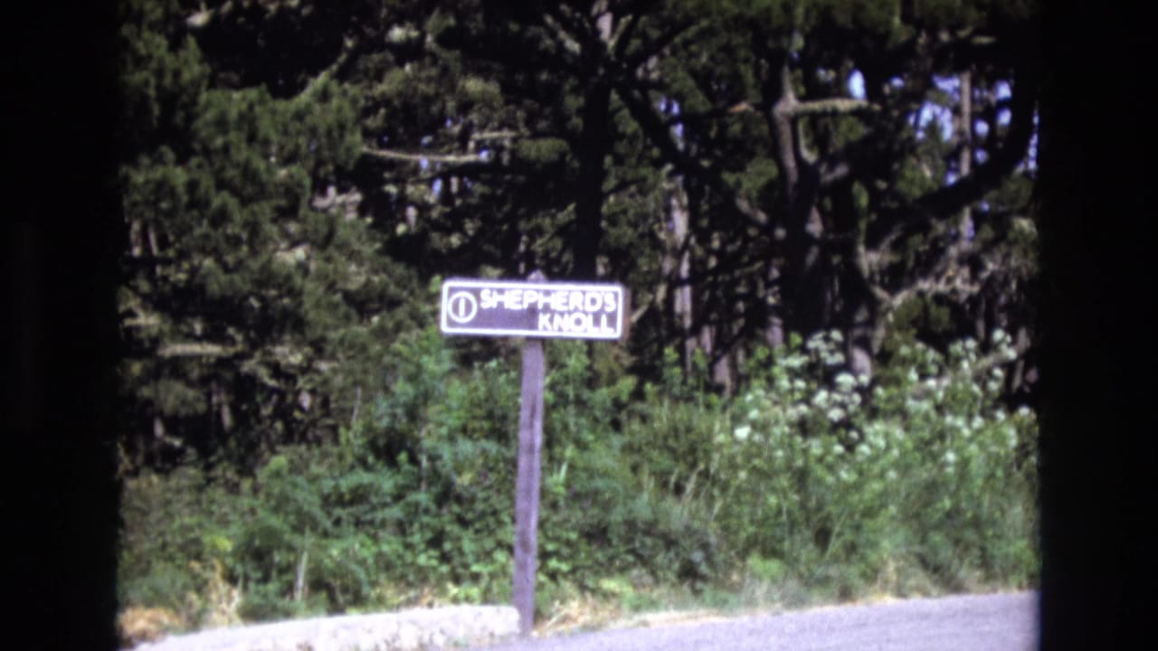 Roadside Shepherd's Knoll sign framed by shrubs, trees, and dark 8mm film edges.