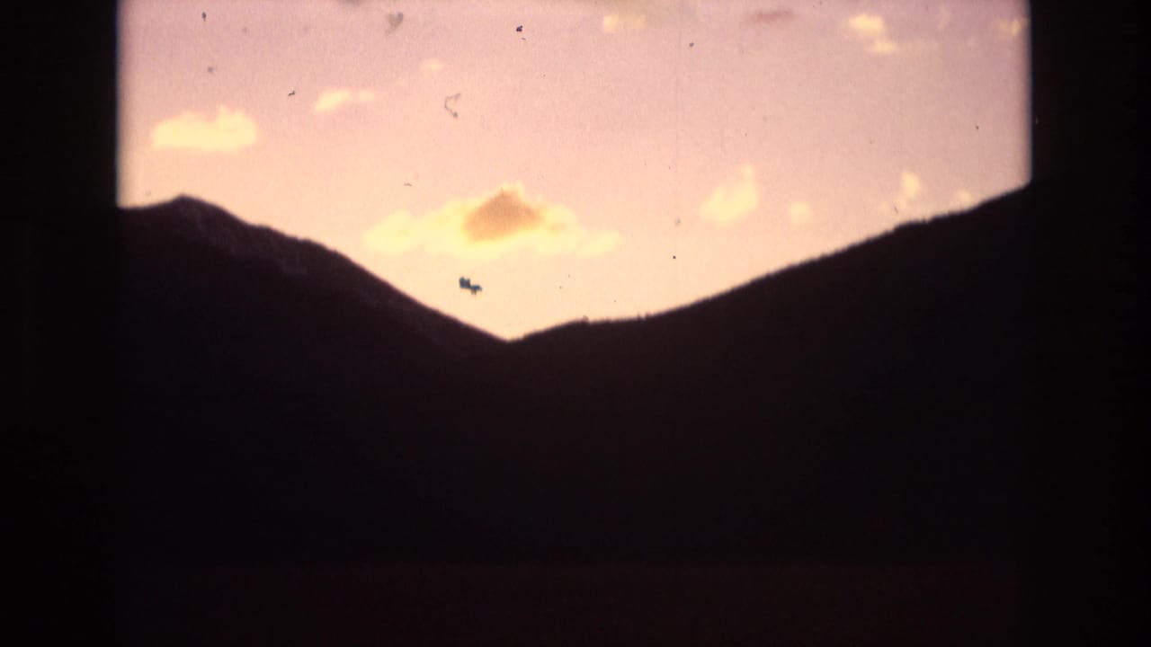 Colorado Springs mountain ridgeline in silhouette beneath a warm orange and pale lavender sky, with small clouds visible inside rounded 8mm frame borders.