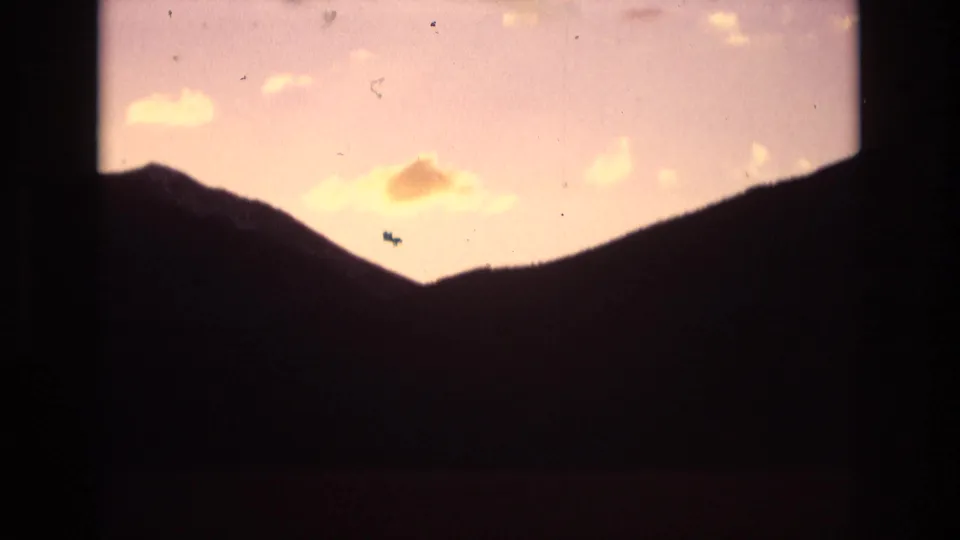 Colorado Springs mountain ridgeline in silhouette beneath a warm orange and pale lavender sky, with small clouds visible inside rounded 8mm frame borders.