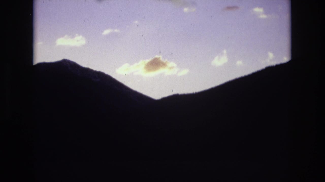 Dark mountain silhouettes beneath a pale dawn sky with small bright clouds.