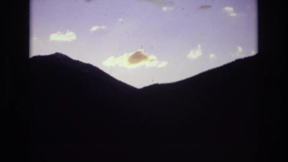 1974 Colorado Springs 8mm frame showing shadowed mountain ridges below a lavender dawn sky with scattered clouds catching early light.