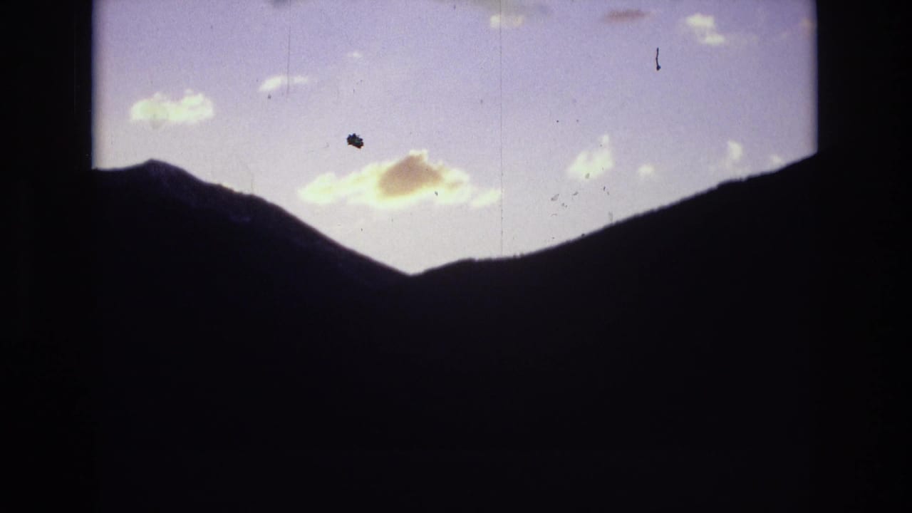 Silhouetted mountain valley with bright dawn clouds against a pale sky.