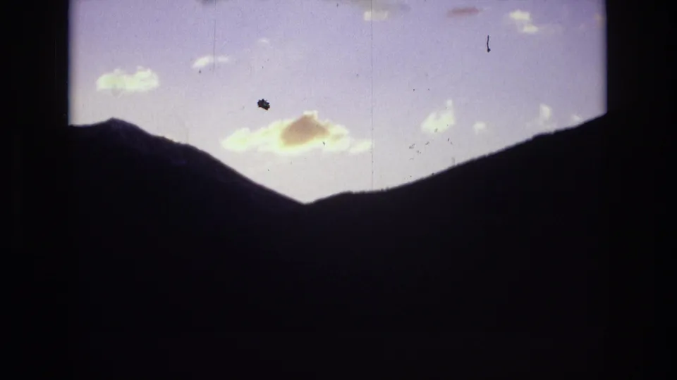 Metadata-supported Colorado Springs sunrise view with dark mountain slopes framing a pale sky and small illuminated clouds on 8mm film.