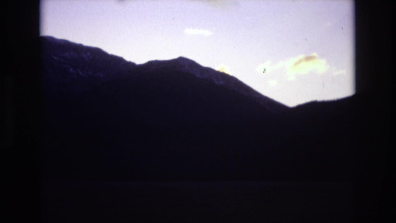 Dark mountain ridge silhouetted against a pale dusk sky with small clouds.