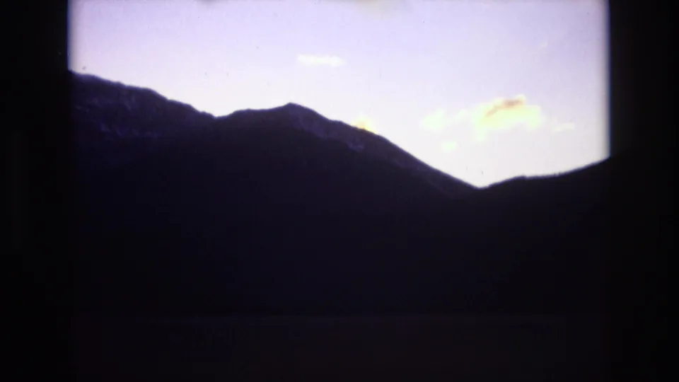 1974 Colorado Springs 8mm frame with a jagged dark ridge line set against a washed lavender evening sky and small illuminated clouds.